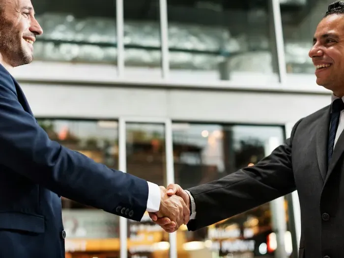 Two professionals smiling and shaking hands outside a building, showing Local Service Connect Now partnerships
